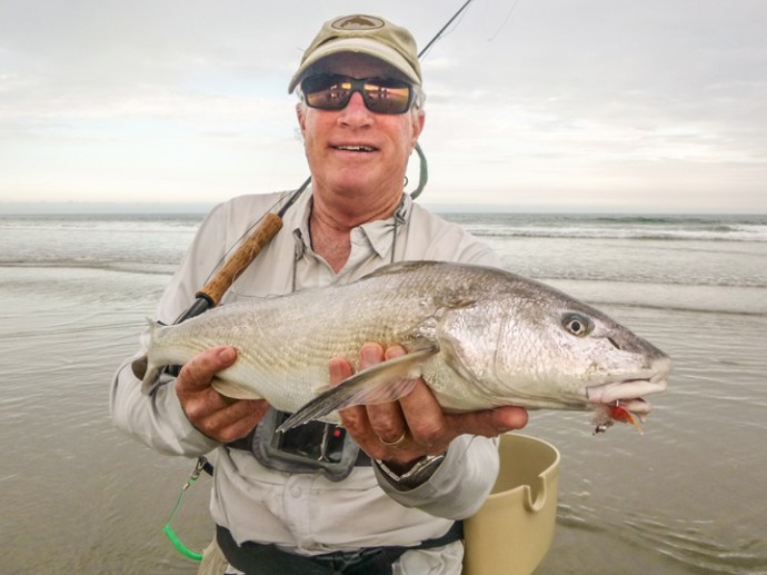 Sometimes everything lines up except the sun. This fish was moving from south to north obviously on the hunt for crabs. It’s back was out and he was on a consistent pattern. First presentation at 60’ was spot on – two feet ahead with a soft landing. It turned and game on! A surprising long battle in the skinny then out to the deep on my 6 weight Z Axis.  Grey colored surfin merkin with an orange butt did the trick. Photo by Jim Solomon.